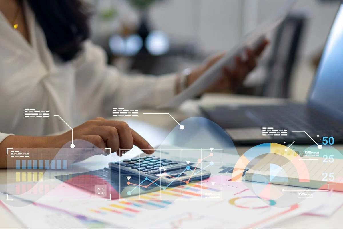 person working at a desk with a calculator and laptop with graphs and charts superimposed over them.
